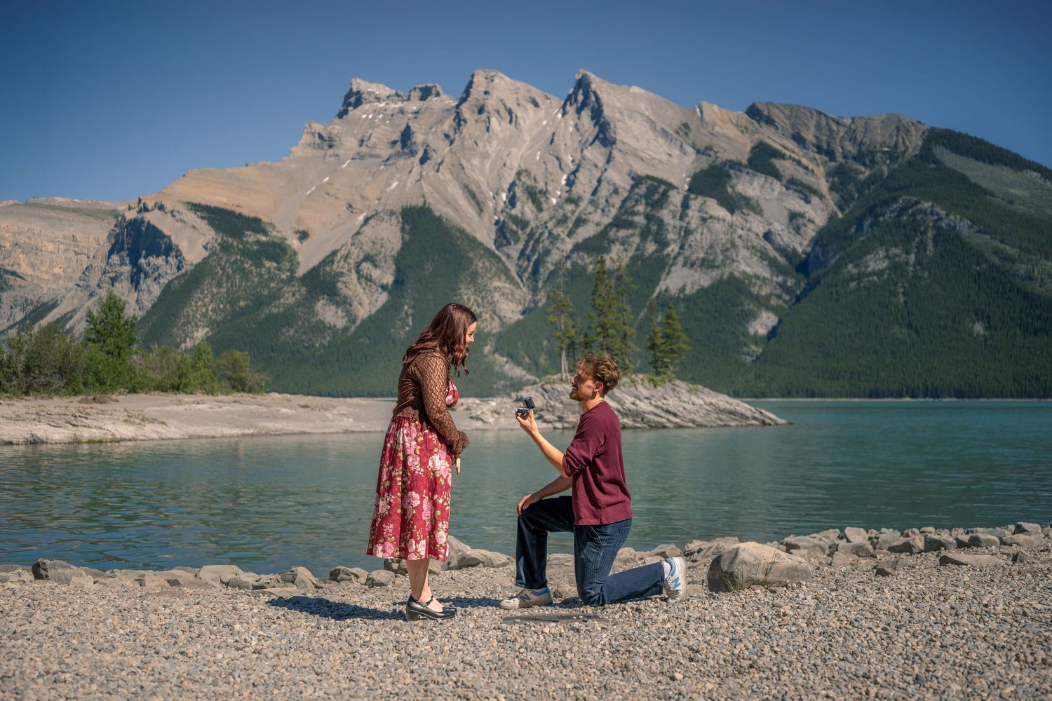 Man proposing to woman on rocky lakeside with stunning mountain backdrop in Banff National Park, Canada.