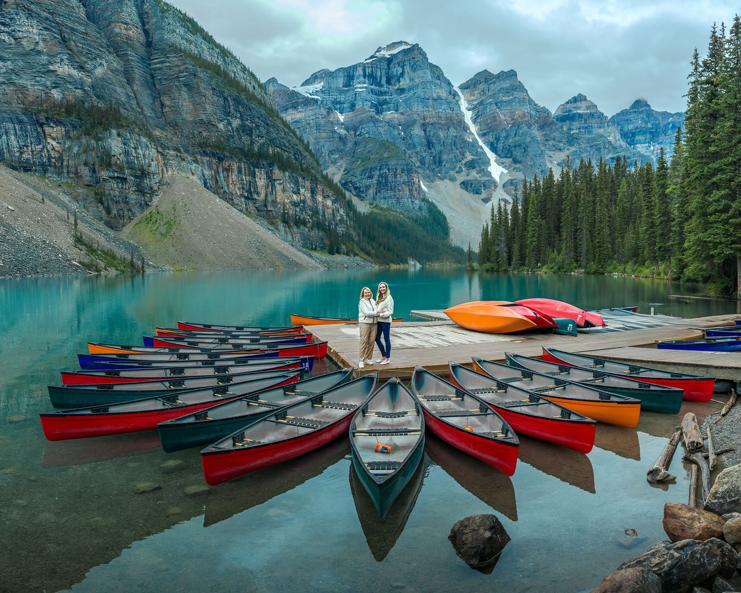 Couple embracing on a dock surrounded by colorful canoes at scenic turquoise Moraine Lake, Banff.