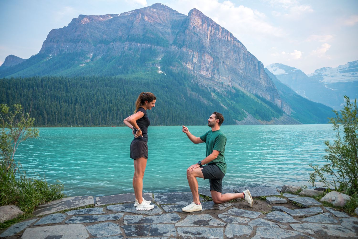 Man proposes on one knee to woman at turquoise Lake Louise with mountain backdrop in Banff National Park.