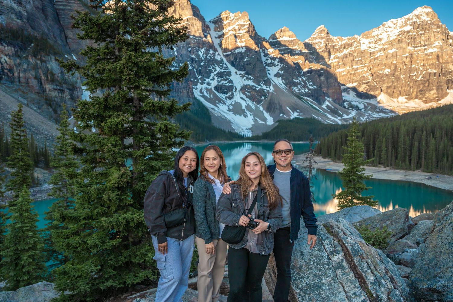 Family of four posing at Moraine Lake with turquoise water and snow-capped Rocky Mountains at sunset.