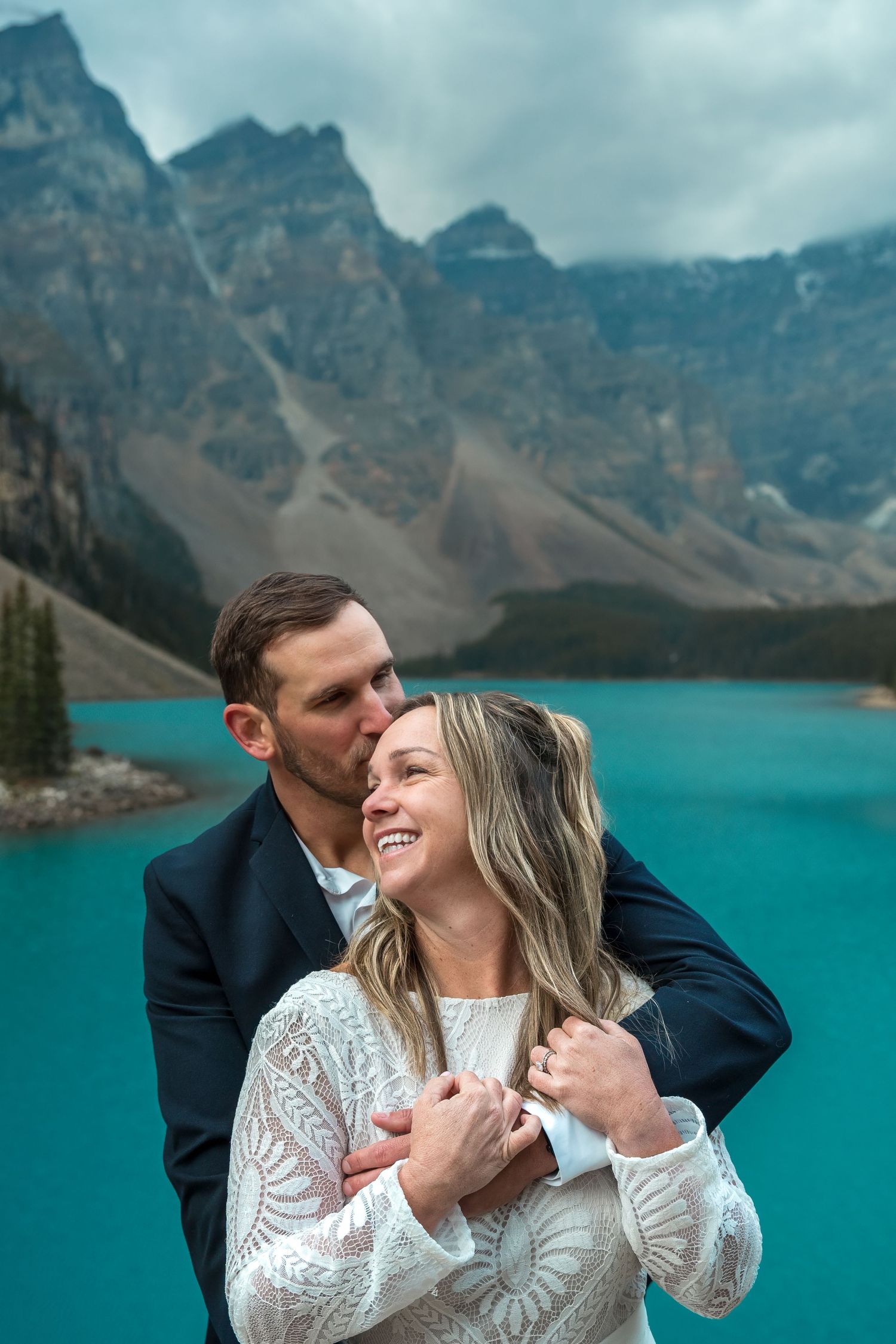 Couple embracing at Moraine Lake, Banff, with turquoise water and Rocky Mountains in the background.