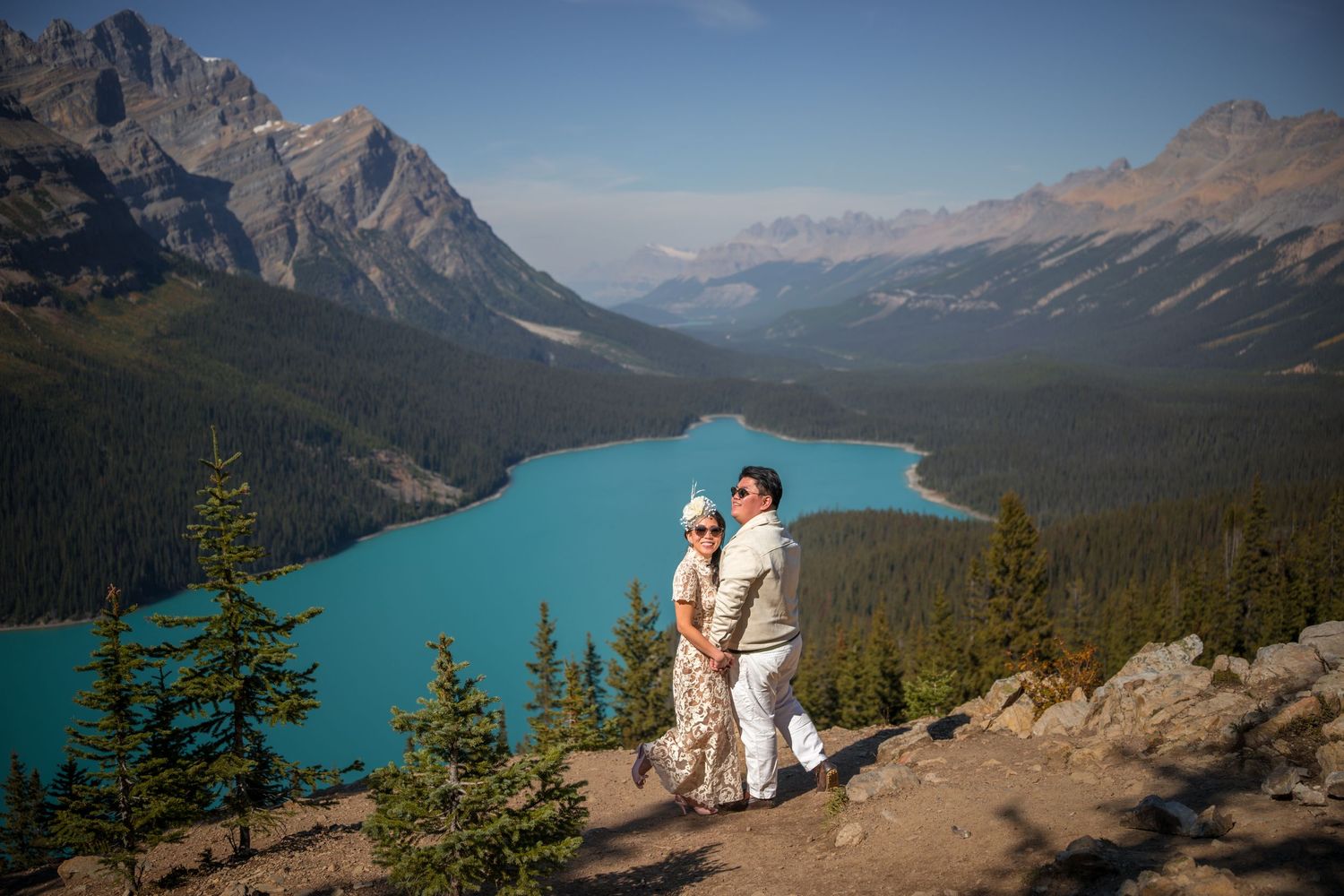 Couple standing on a rocky overlook above turquoise Peyto Lake surrounded by mountains in Banff National Park.