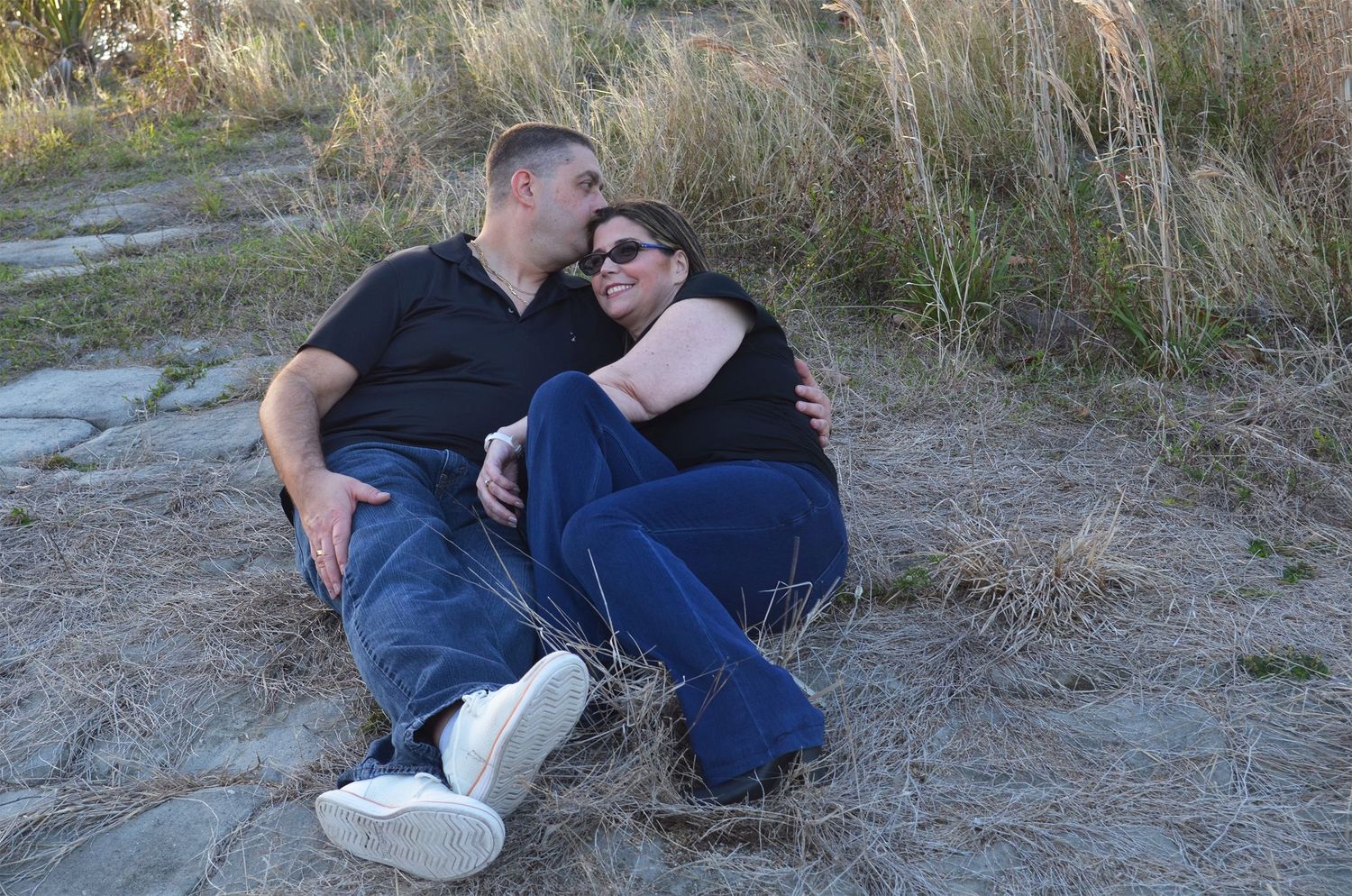 Couple sitting together in tall dry grass outdoors.