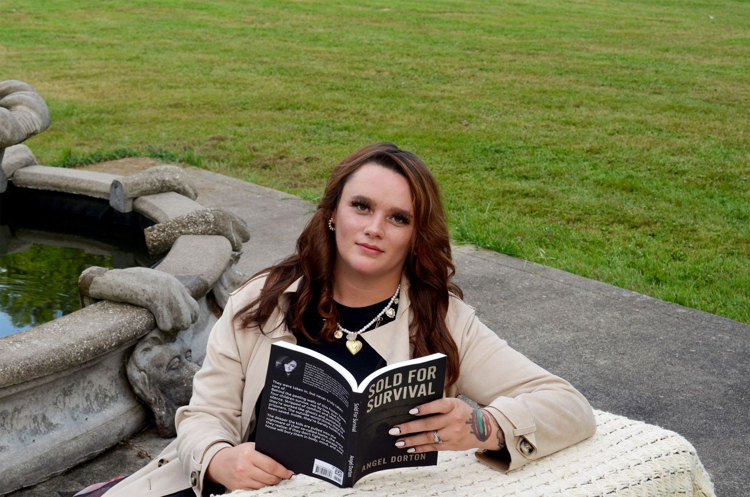 Author holding book outdoors near fountain.