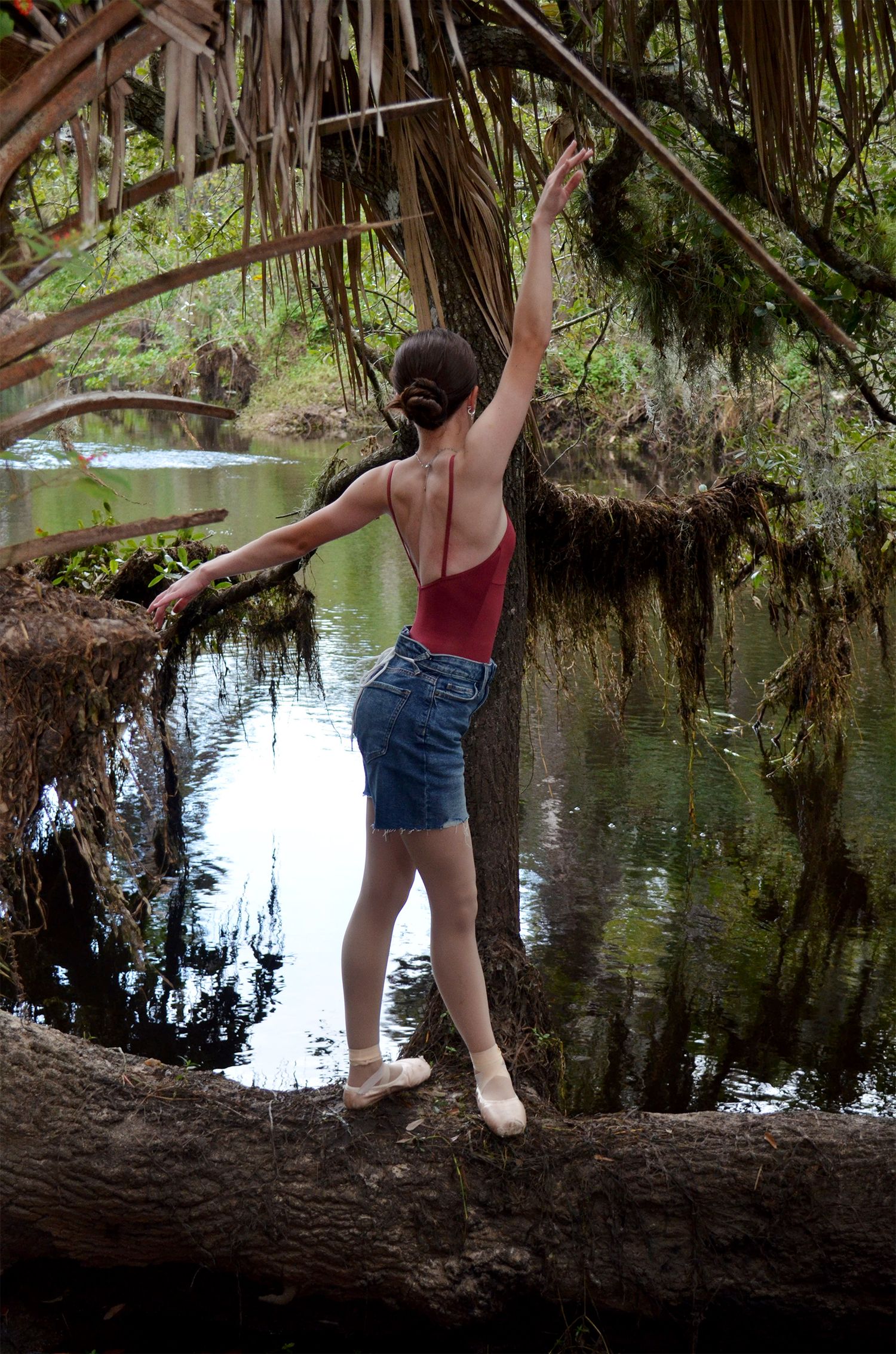 Ballet dancer balancing on a fallen log in a forest river.