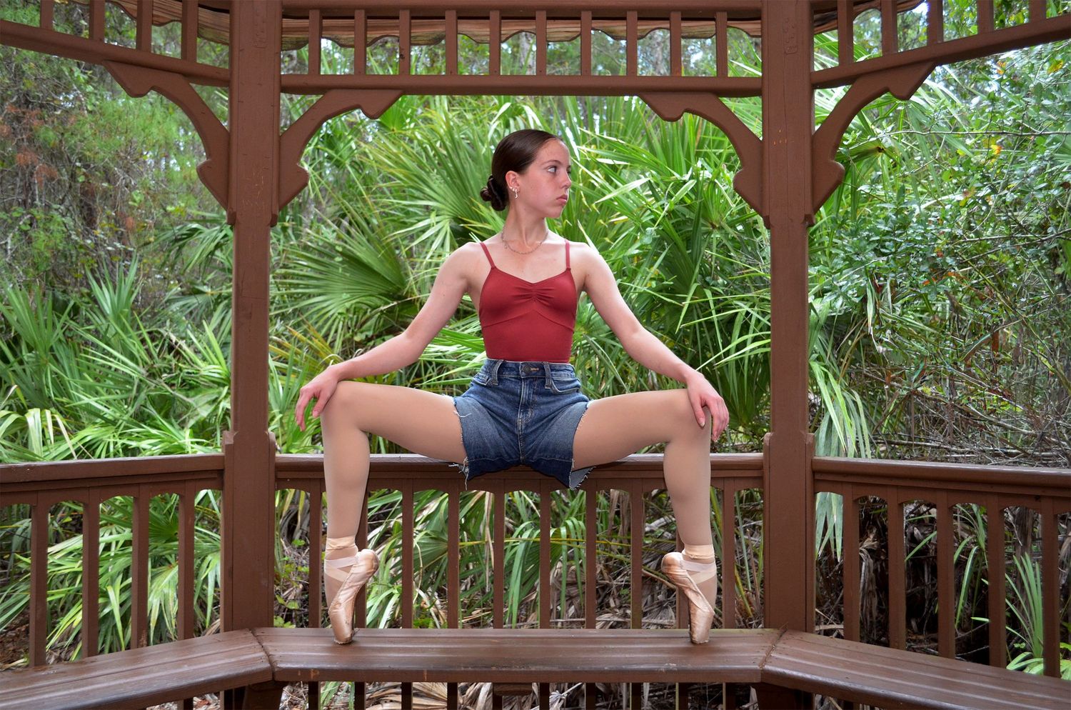 Ballerina holding a grand plié on pointe in a wooden gazebo.
