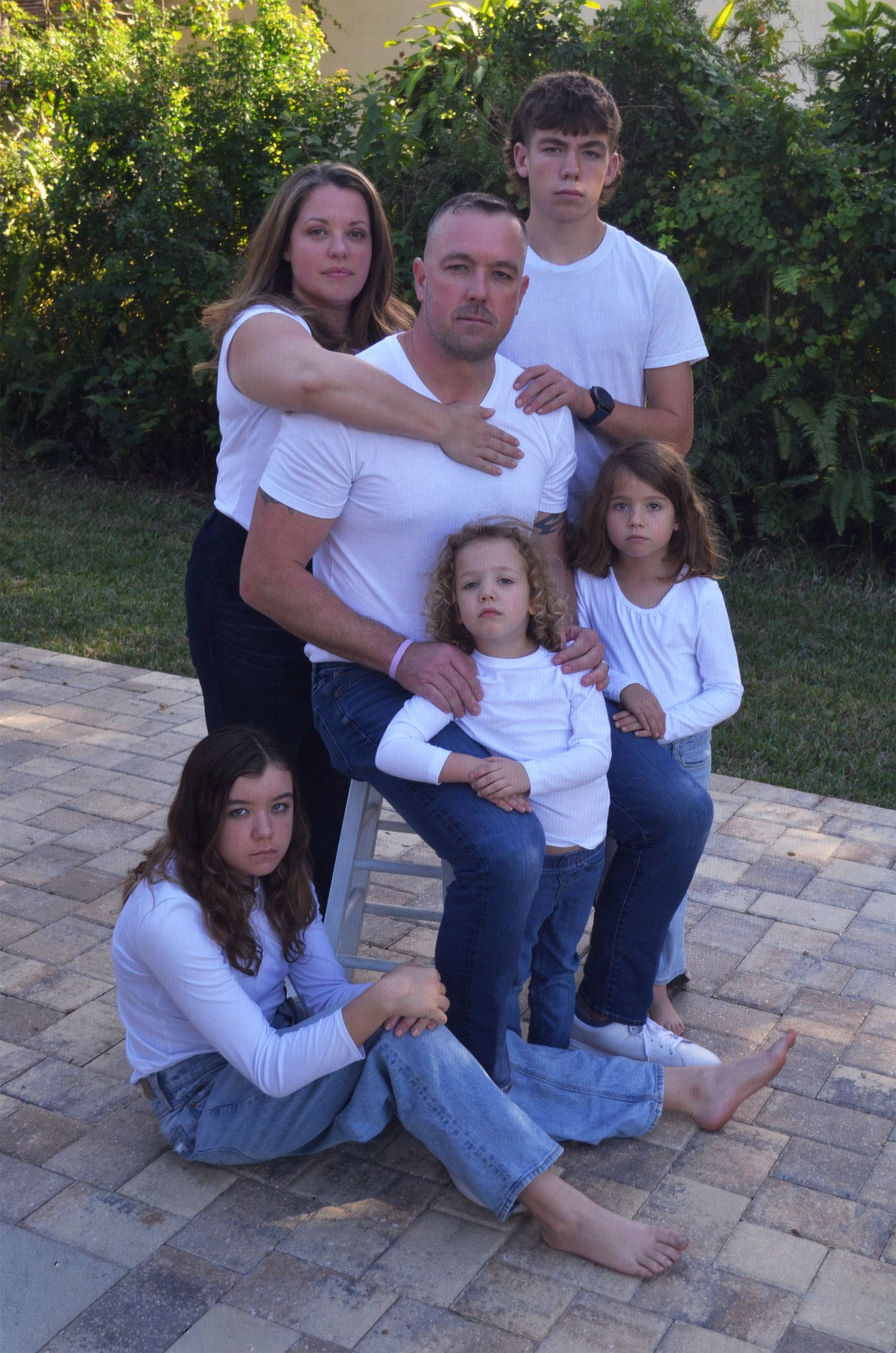Family of six posing in matching outfits on brick patio.