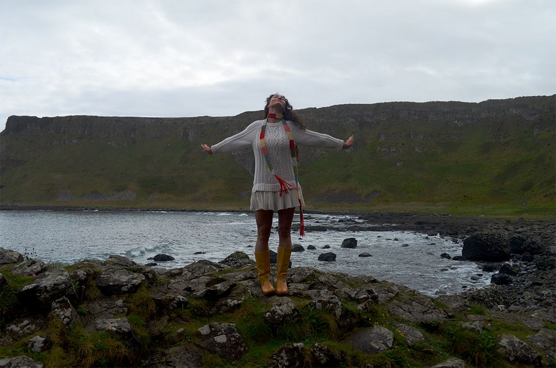 Woman standing on coastal cliffs with arms outstretched.
