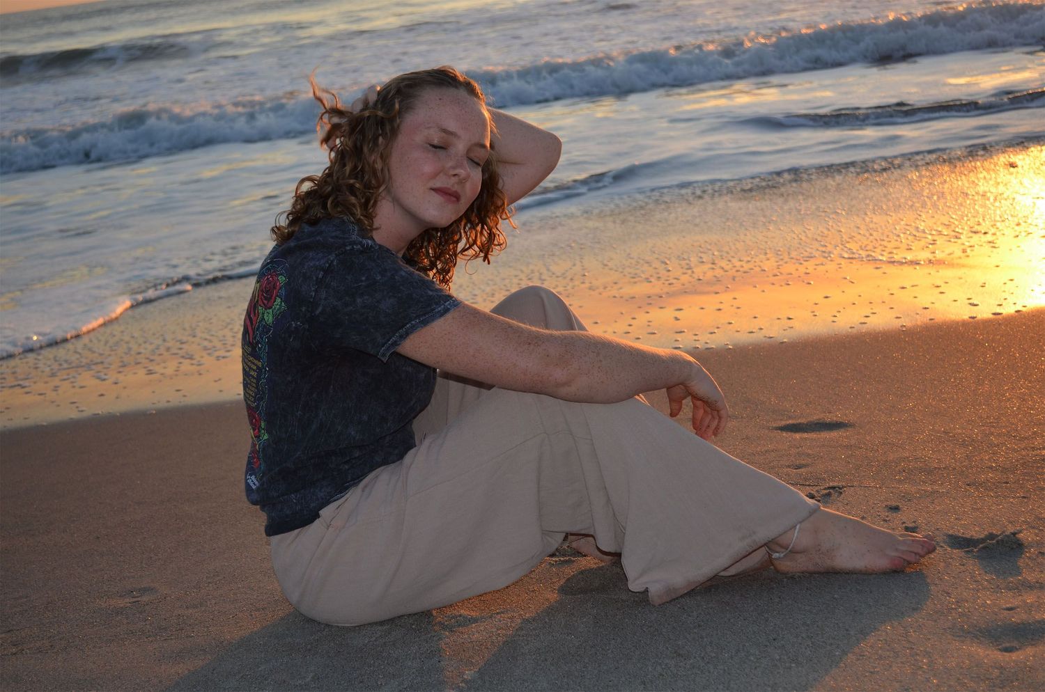 Teenage girl sitting on beach at sunrise with ocean behind her.