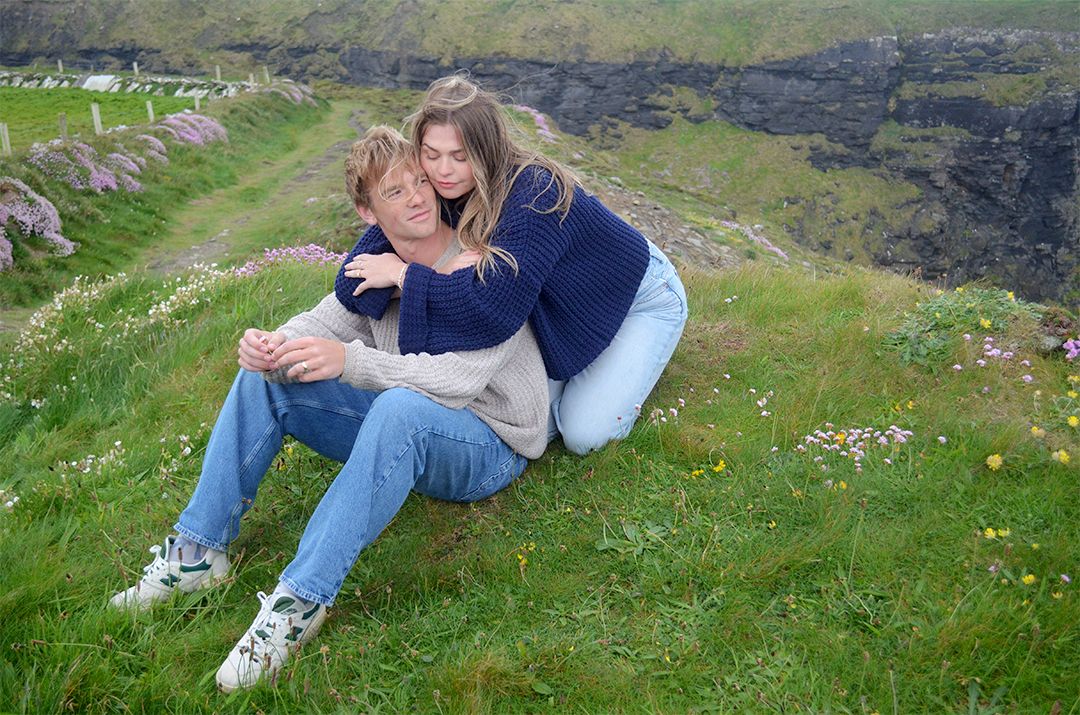 Couple laughing on grassy hillside near coast.