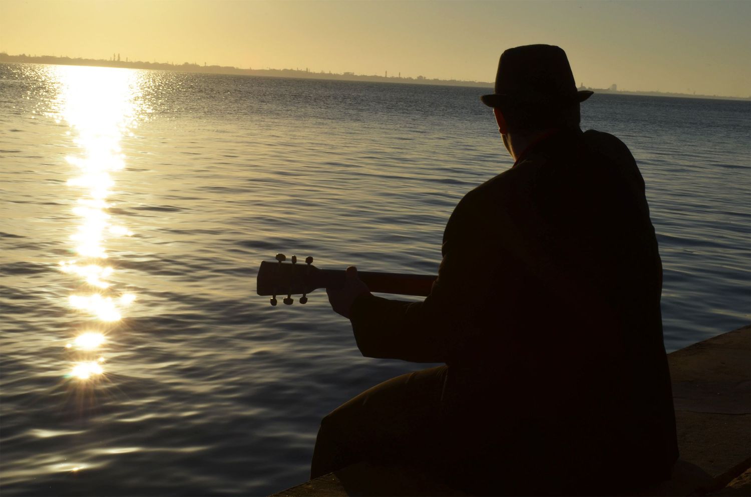 Silhouette of teenage boy by water at sunrise.