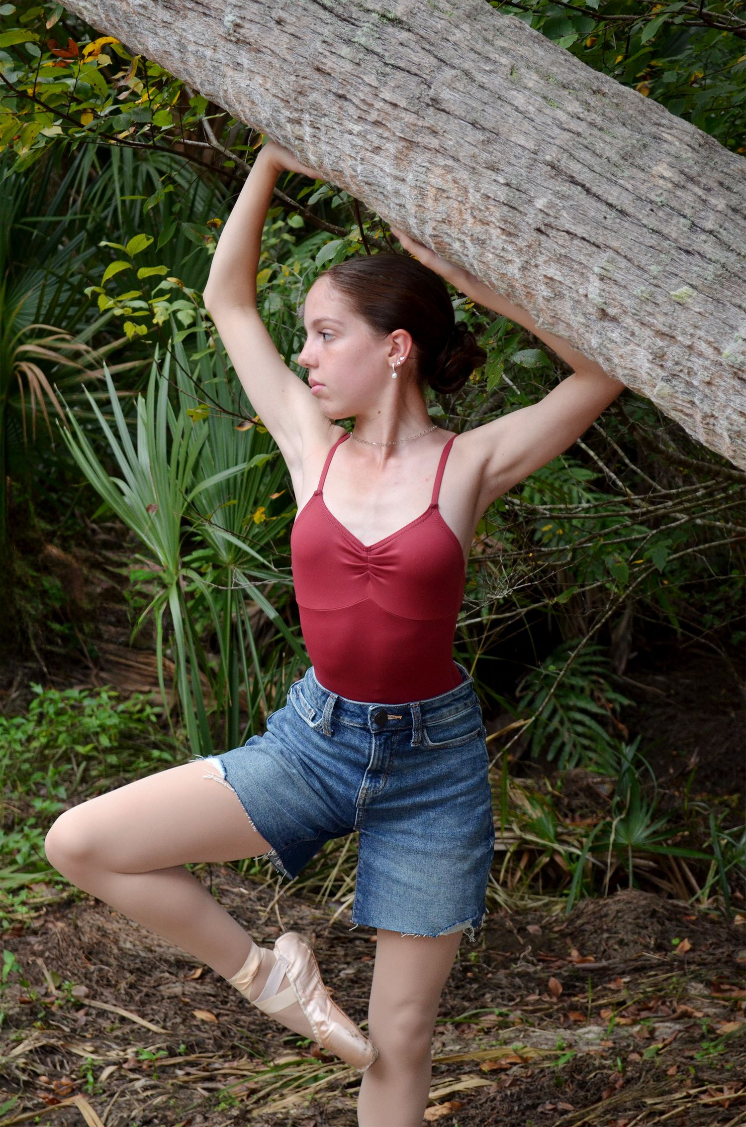 Ballet dancer balancing on one leg beneath a fallen log in greenery.