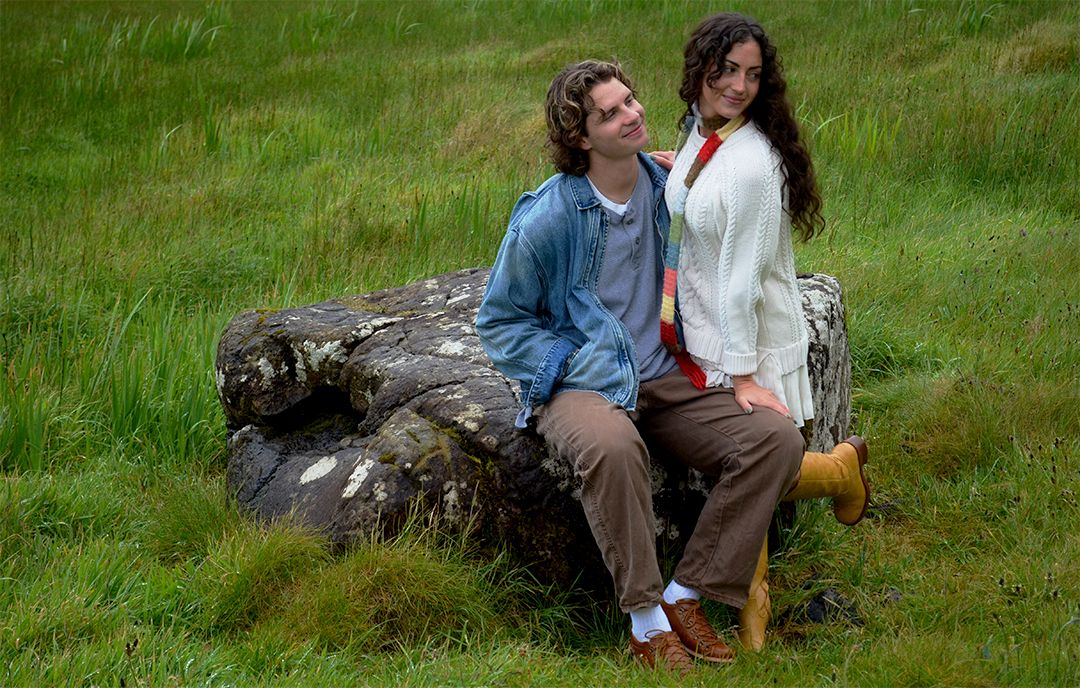 Couple leaning together in grassy field.