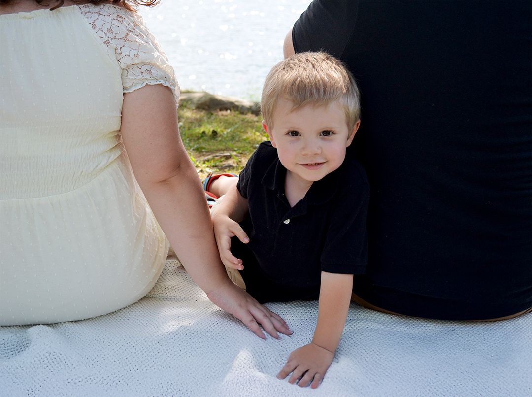 Toddler sitting between parents on blanket near water.