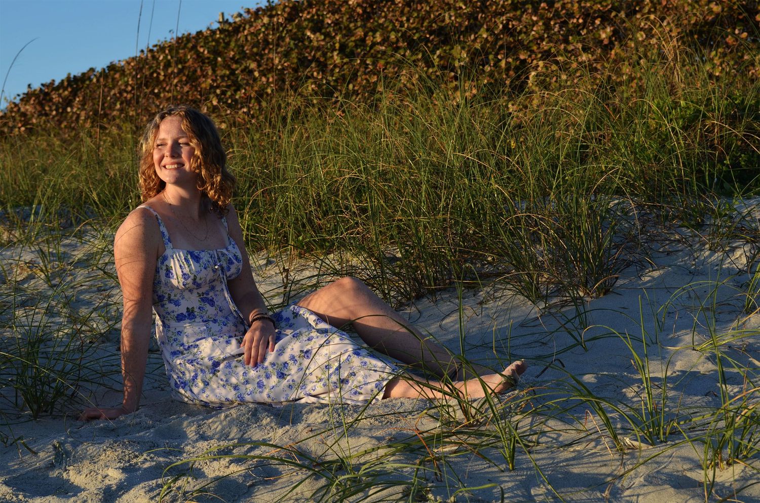 Teenage girl sitting barefoot on sandy dunes at golden hour.