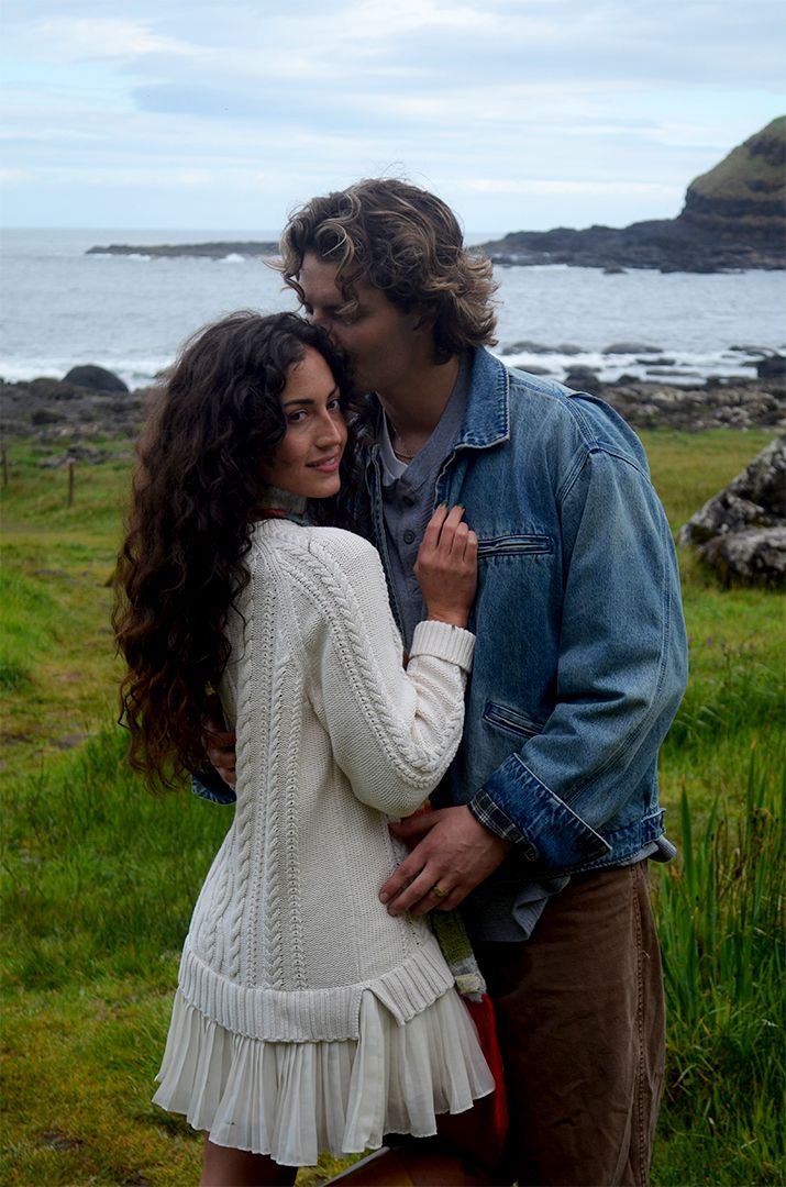 Couple posing on stone cliffs overlooking sea.