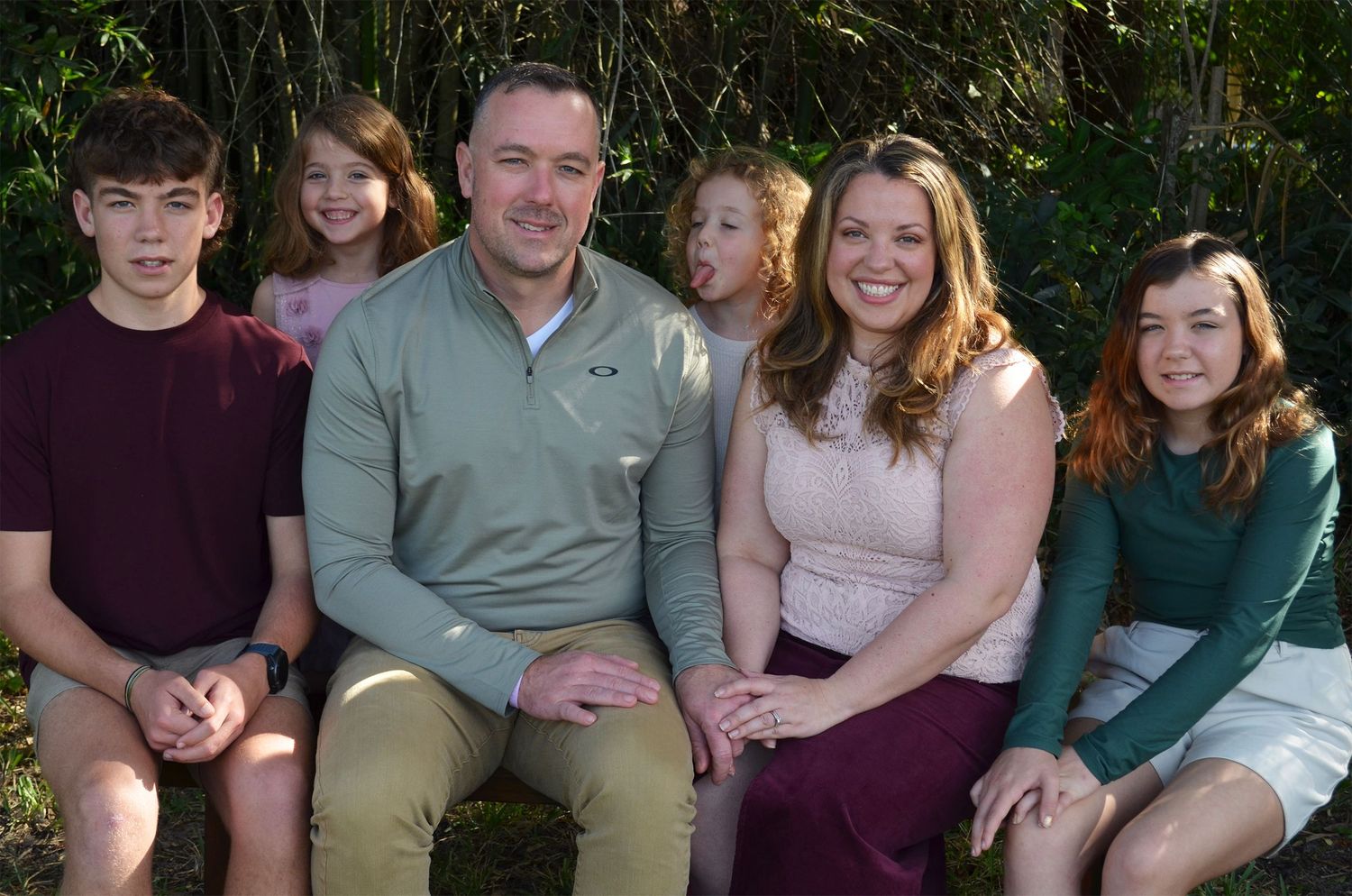 Family of six smiling together outdoors among greenery.