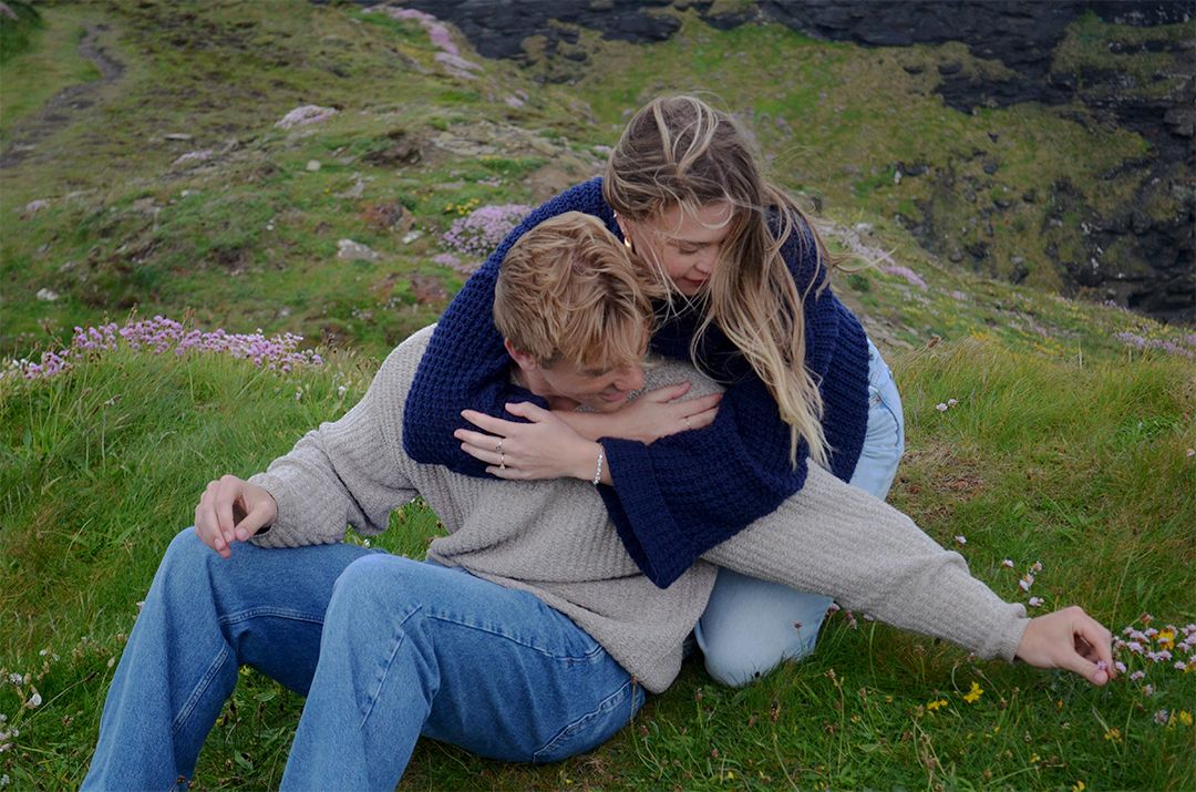 Couple embracing in green field near cliffs.