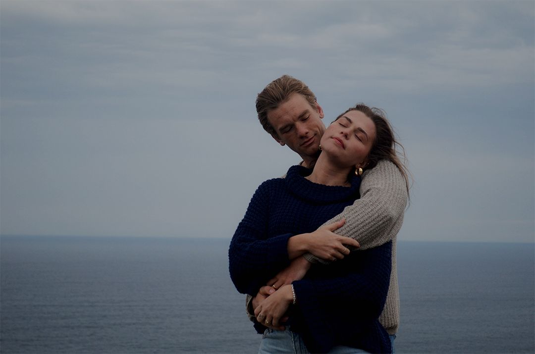 Couple embracing by ocean on cloudy day.