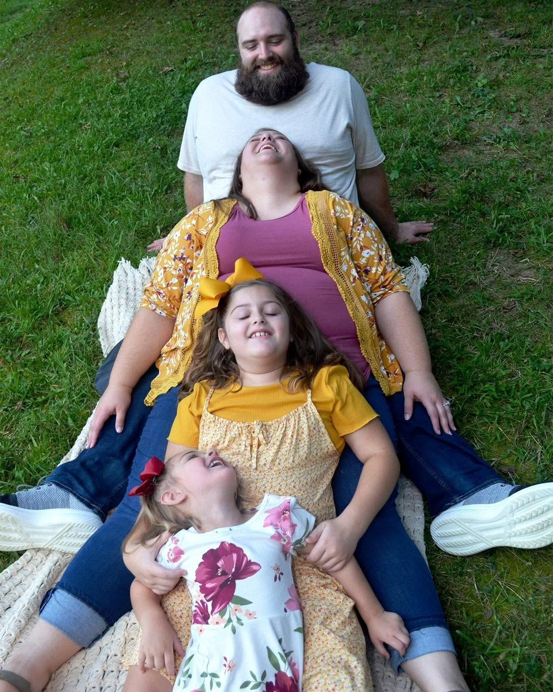 Happy family of four sitting together while laughing during outdoor portrait session.