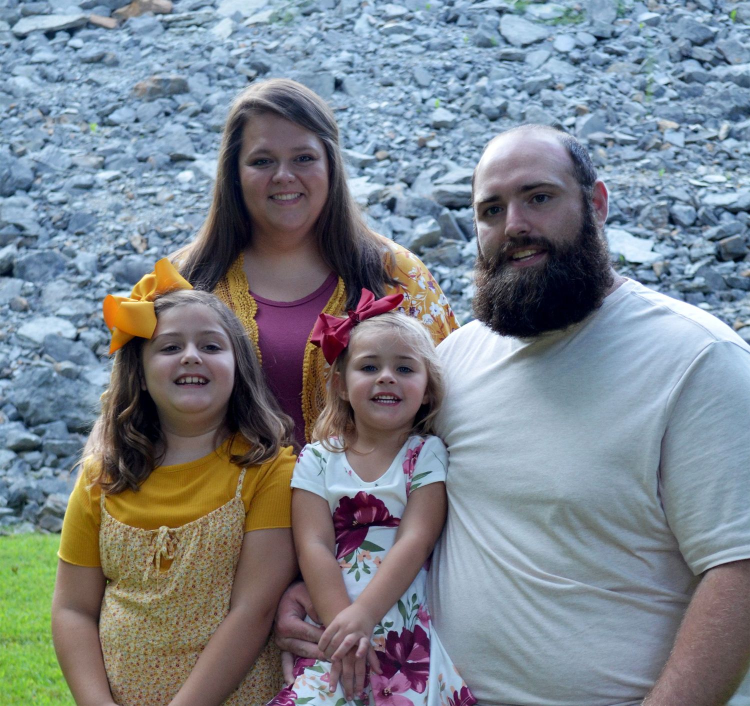 A smiling family of four poses outdoors near rocky terrain.