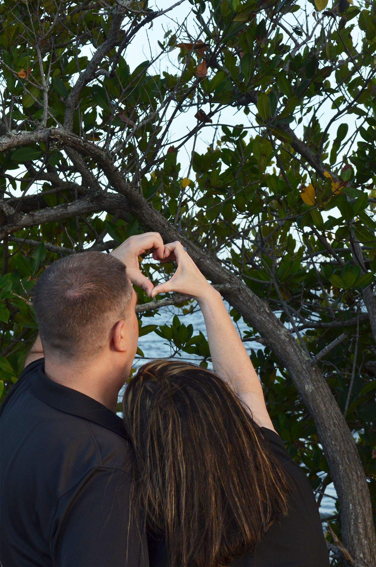 Couple making heart shape with hands outdoors.
