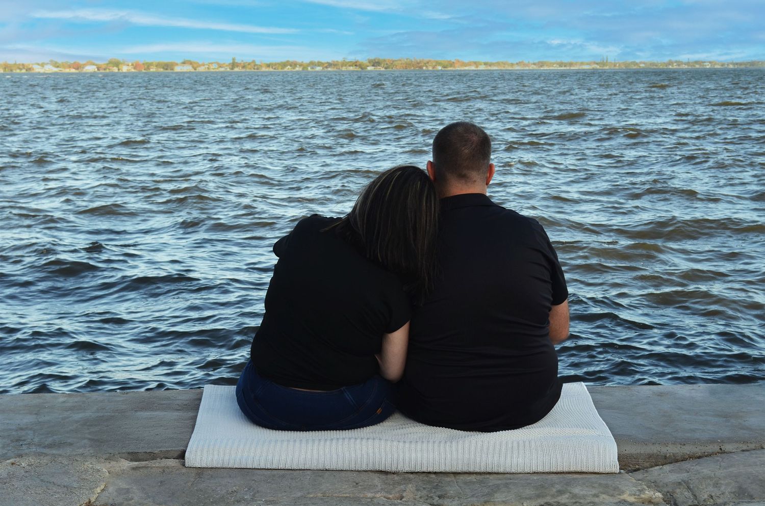 Couple sitting on waterfront dock looking toward ocean.