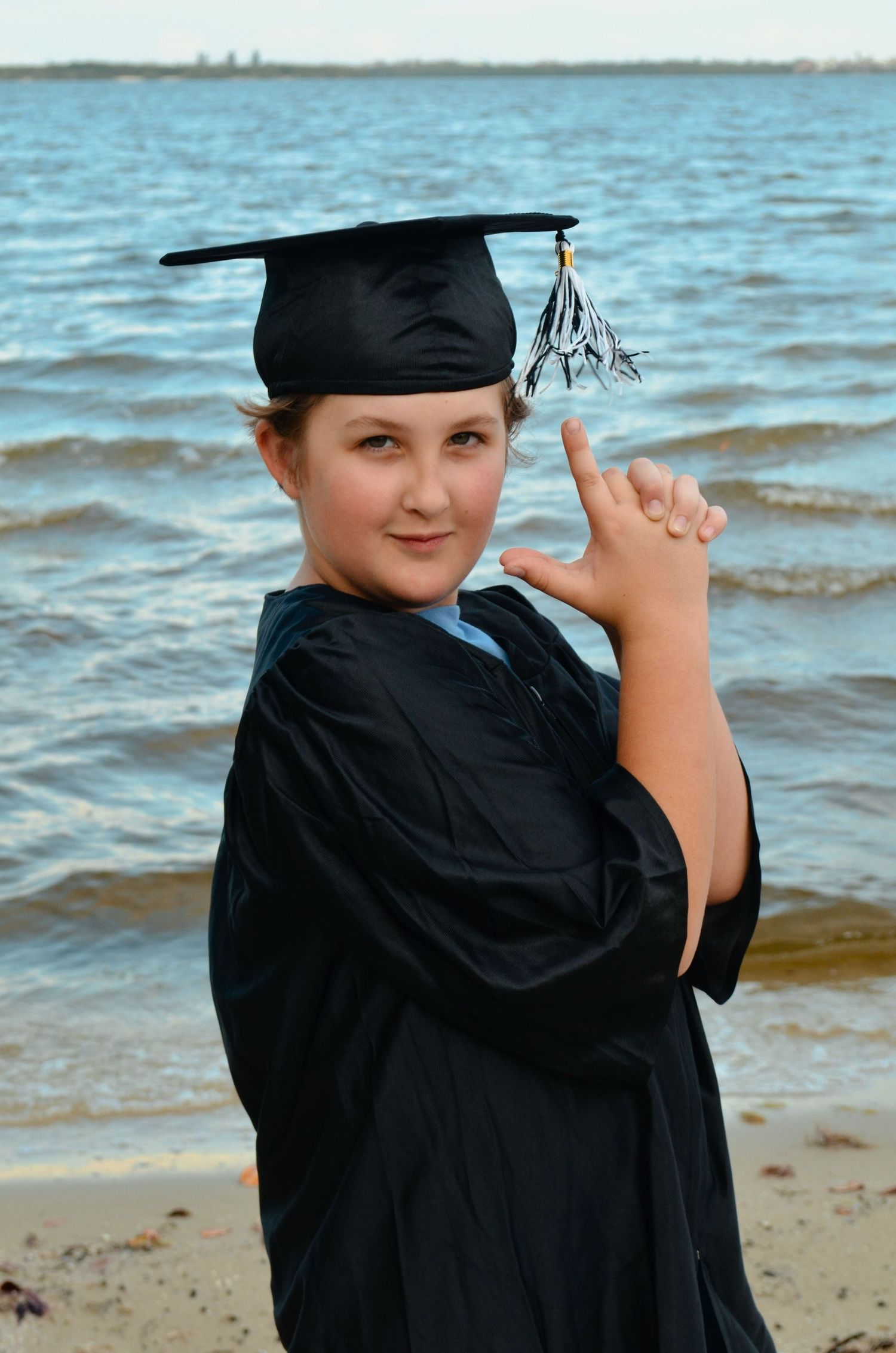 Young boy in graduation cap and gown posing on shoreline.