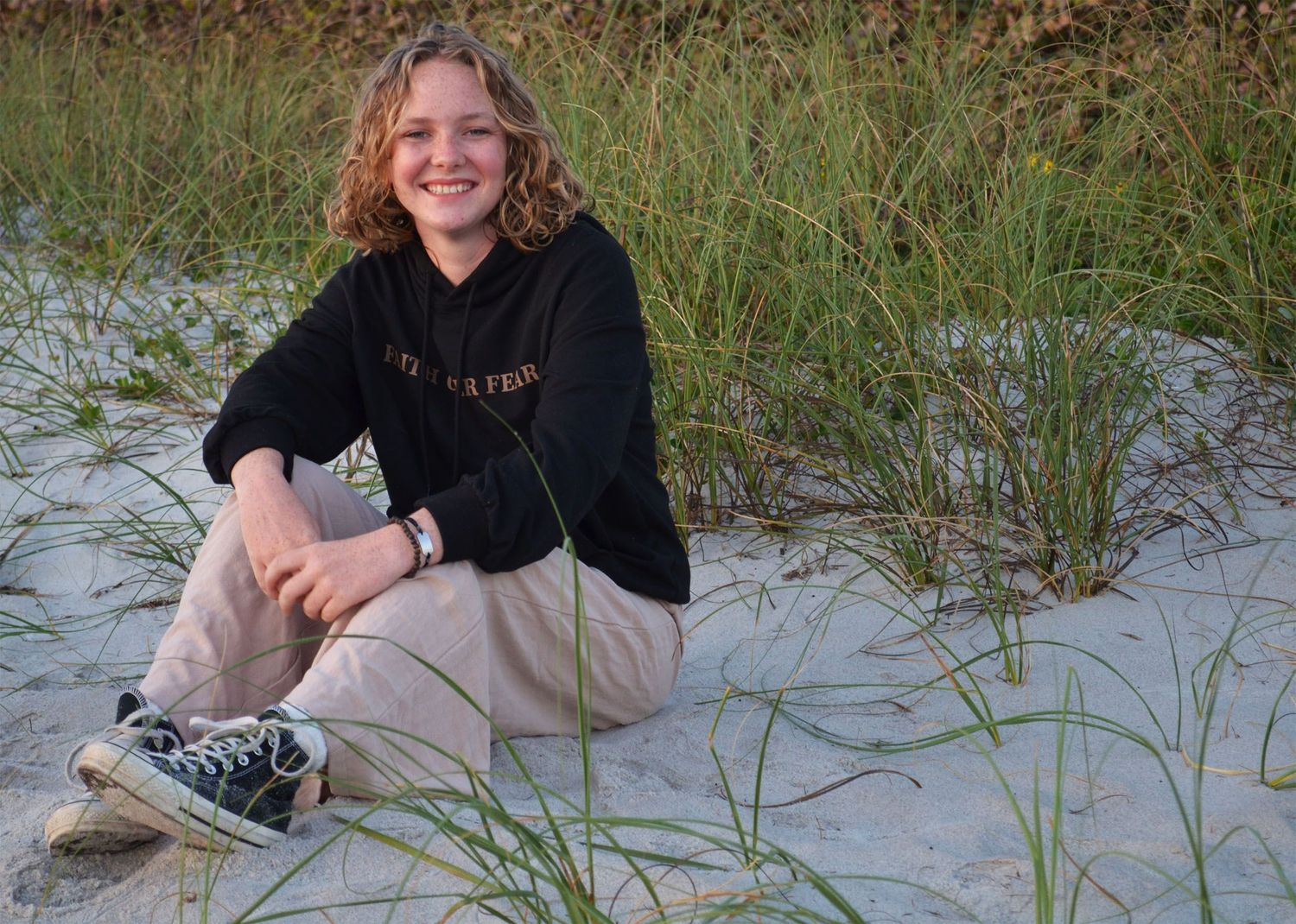 Teenage girl sitting among coastal grass on beach.
