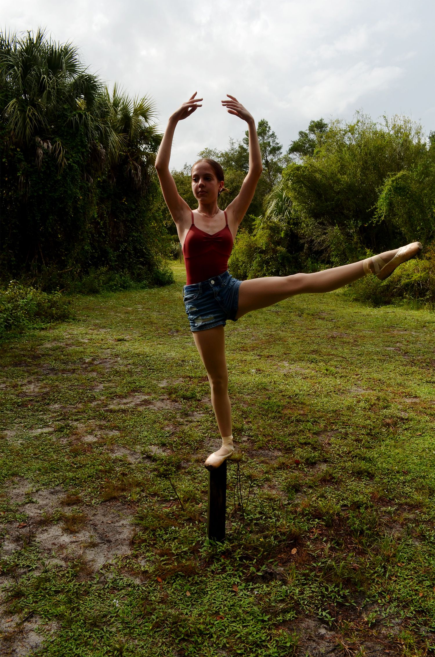 Ballet dancer performing an arabesque in a green field.