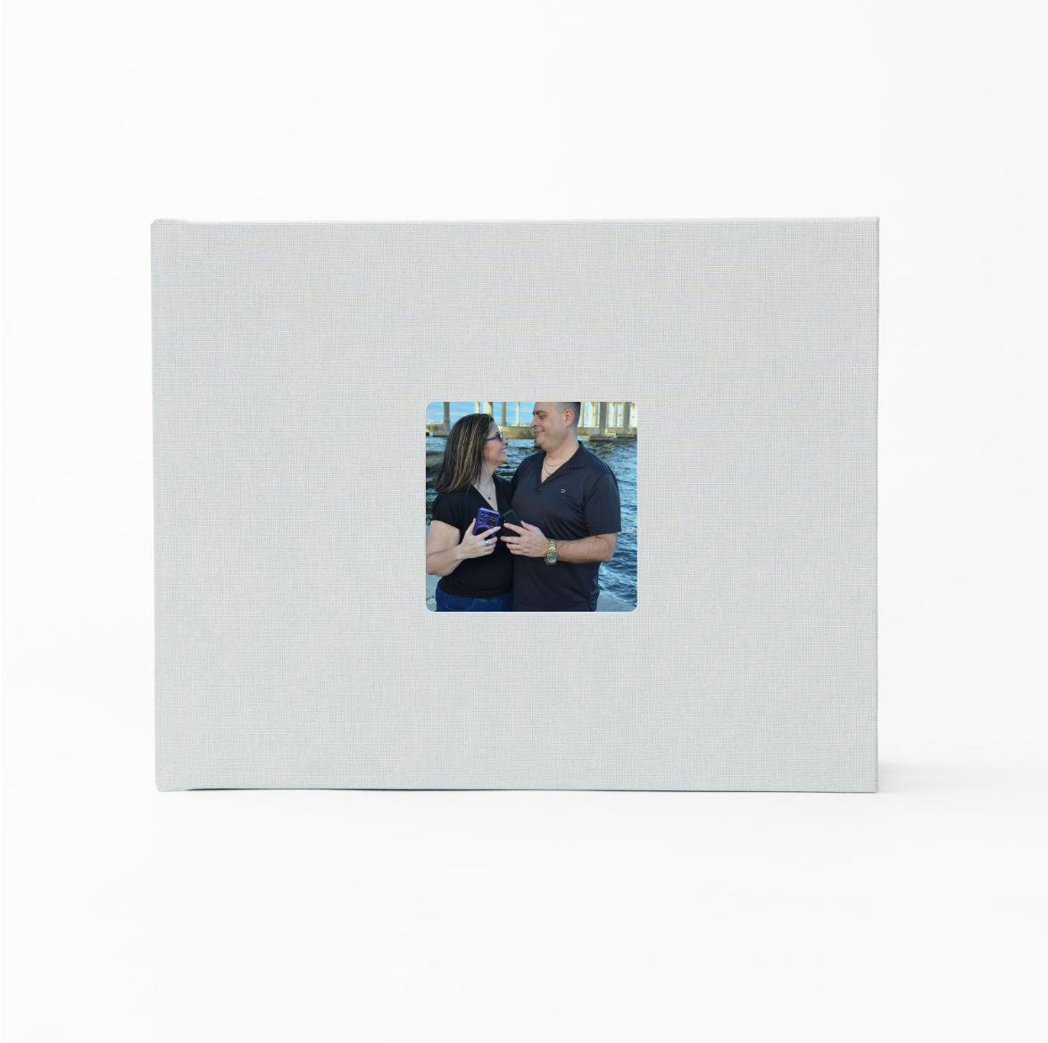 White linen photo album with square window displaying a couple in black outfits smiling at each other.