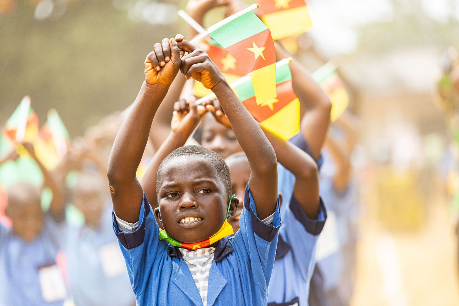 African schoolchildren in blue uniforms waving colorful flags during an outdoor celebration.