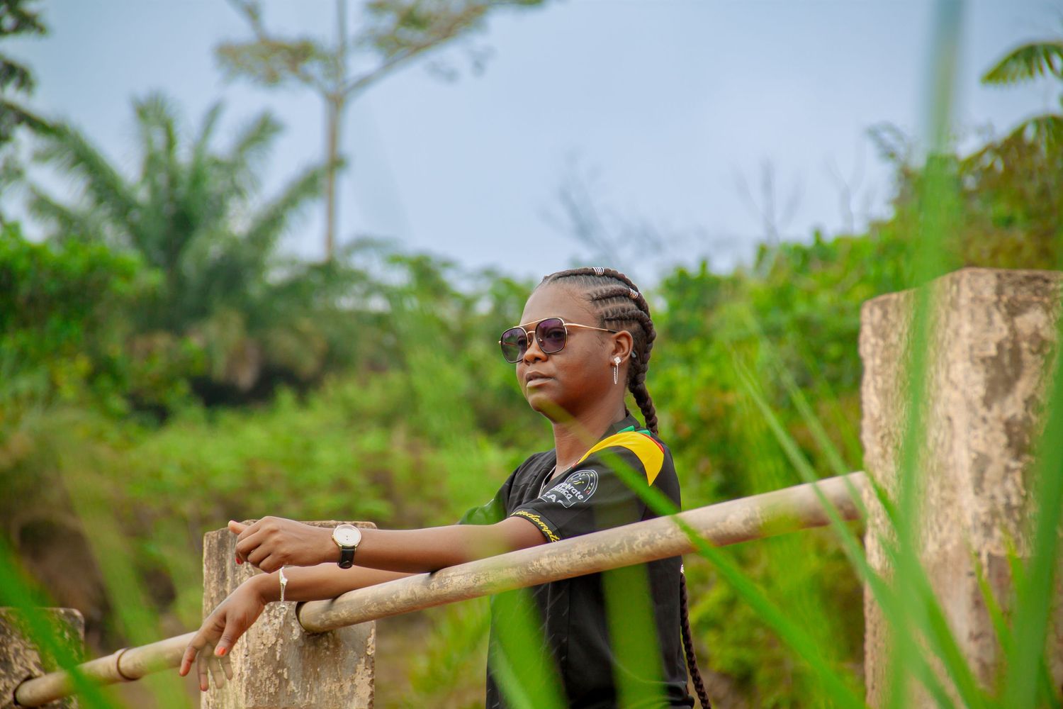 Person in sunglasses resting on wooden fence in tropical outdoor setting.