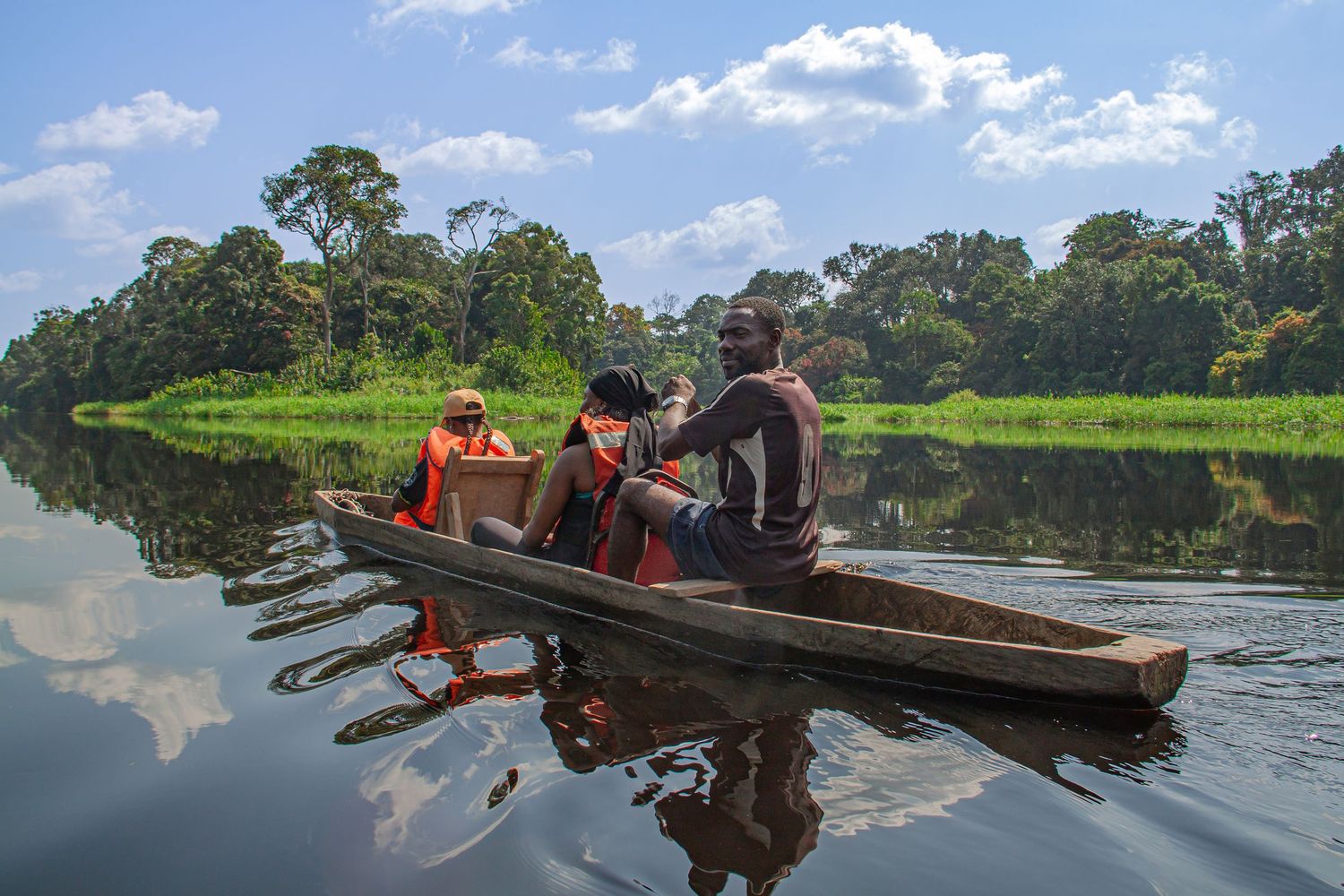 Three people paddling a traditional wooden canoe on a calm jungle river in Africa.