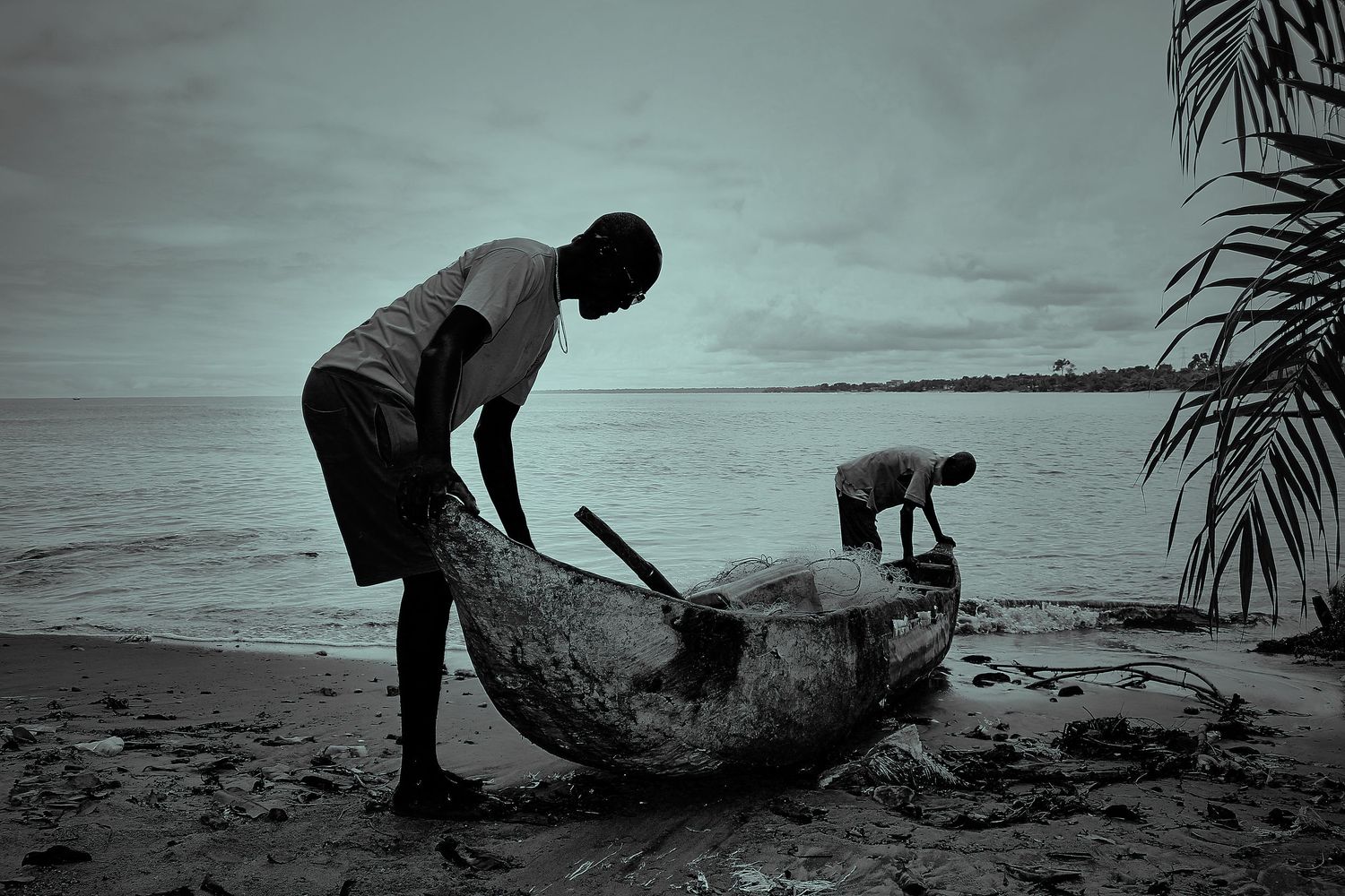 Two fishermen working on a dugout canoe on an African beach in black and white.