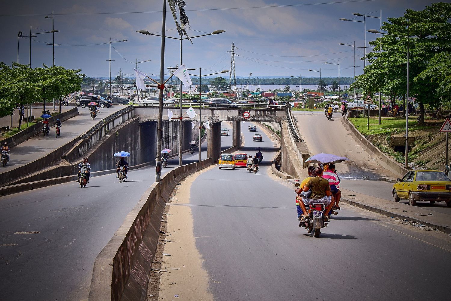 Busy urban road with underpass tunnel, motorcycles, and cars in a tropical African city on a sunny day.