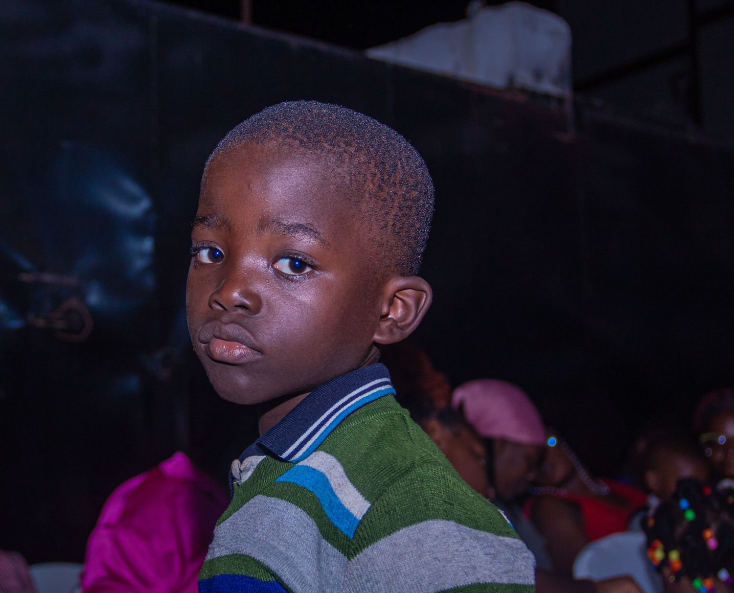 Young African boy in a striped polo shirt looking over his shoulder in a colorful setting.