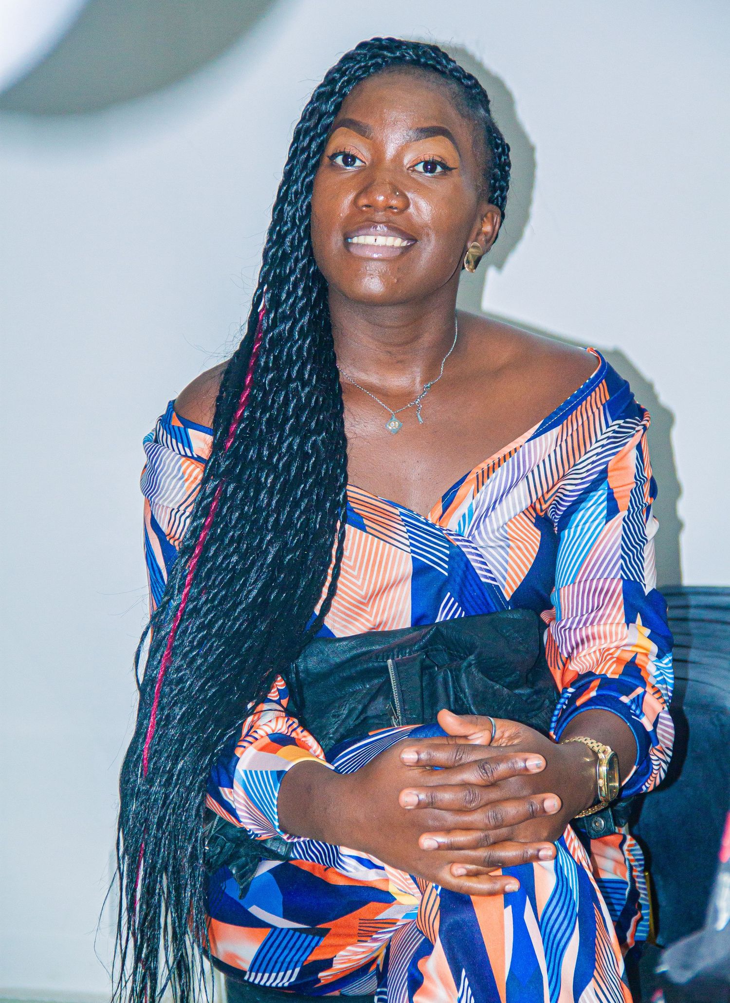 Smiling African woman with long braids wearing colorful off-shoulder patterned dress.