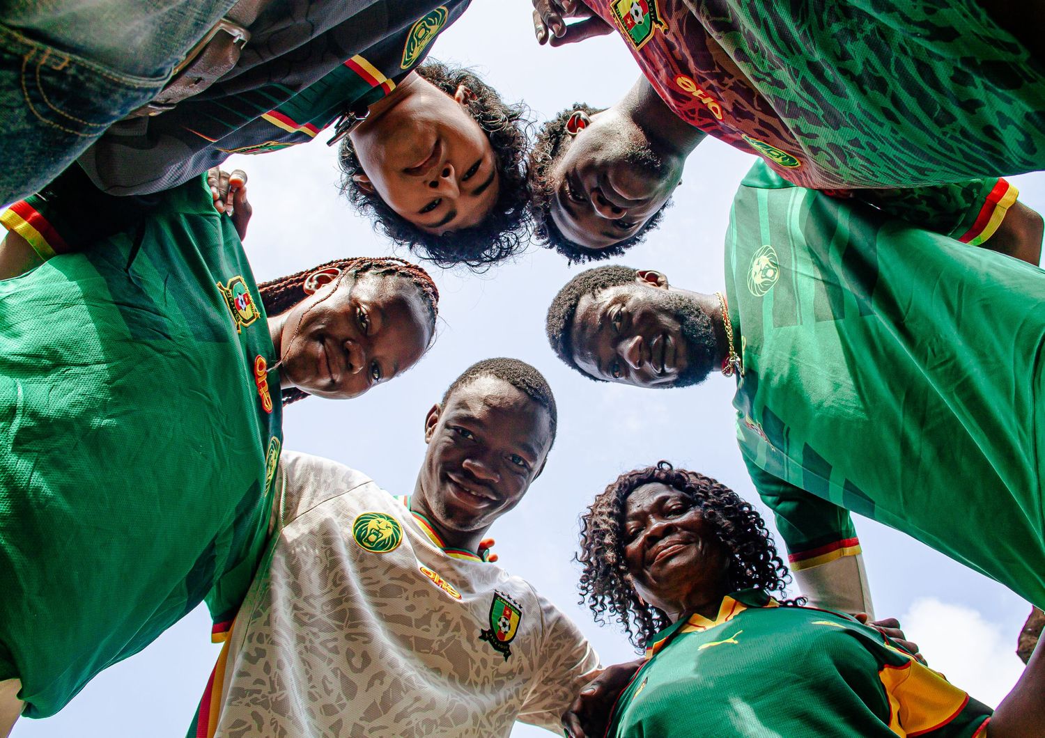 Low angle view of African friends in Cameroon jerseys huddled together smiling.