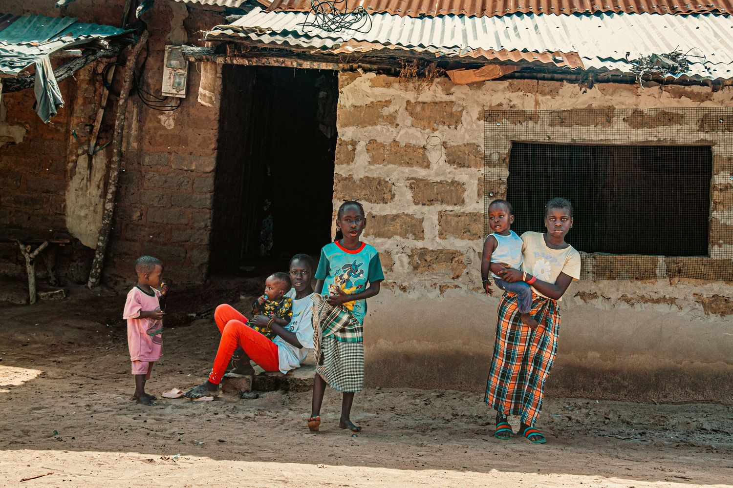 African women and children standing outside a weathered brick building in a rural village.