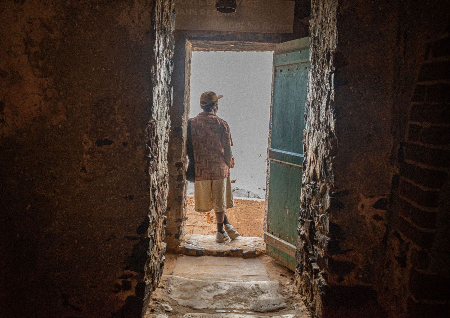 A silhouetted figure stands in a doorway of a historic stone building, holding a bag on Goree Island.