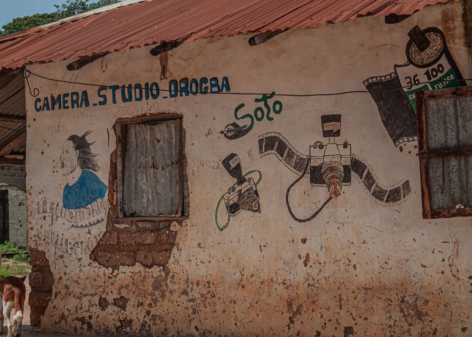 Weathered wall of Camera Studio Orogba painted with retro film and camera murals in an African village.