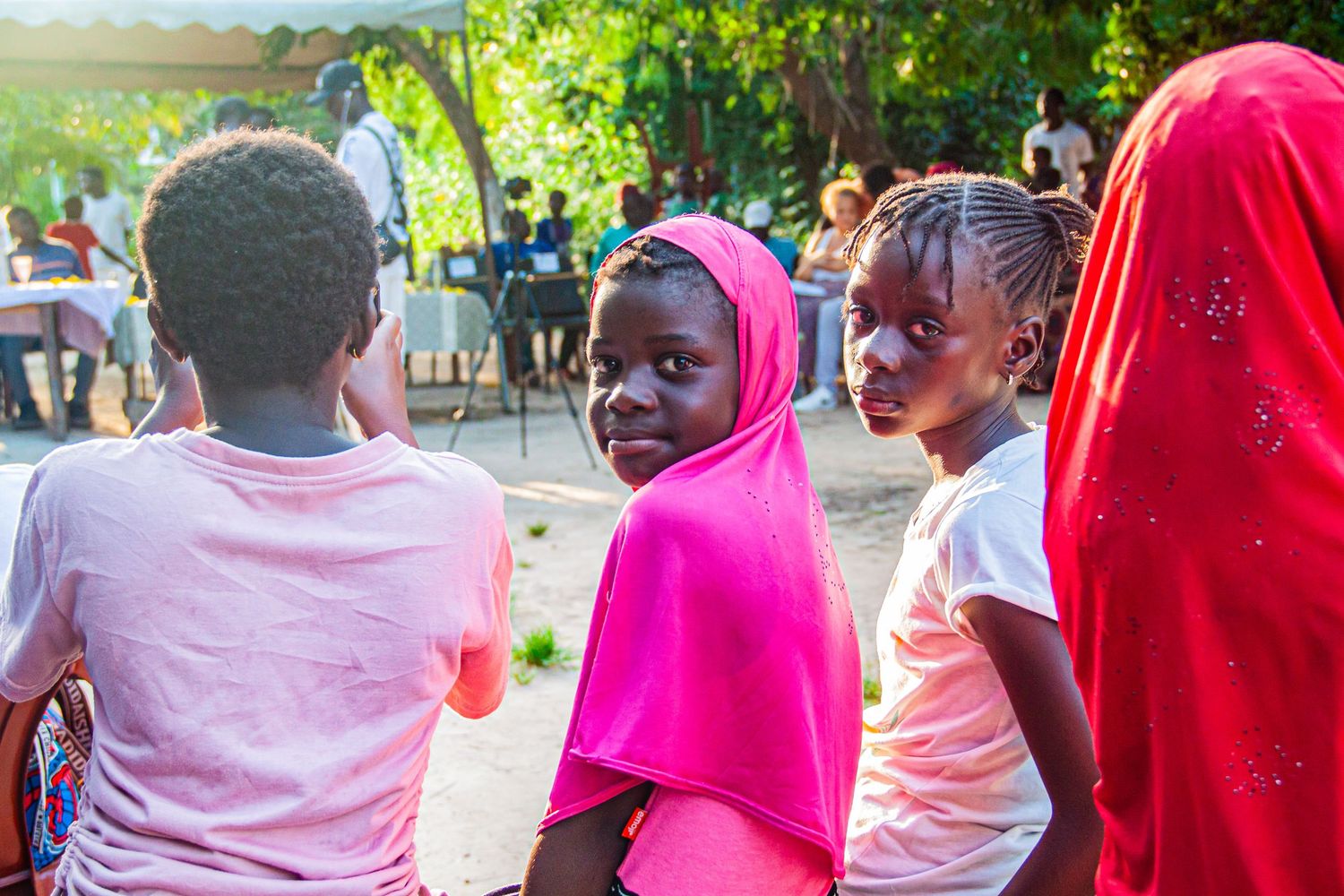Young African girls in pink headscarves and casual clothing gathered at an outdoor community event.