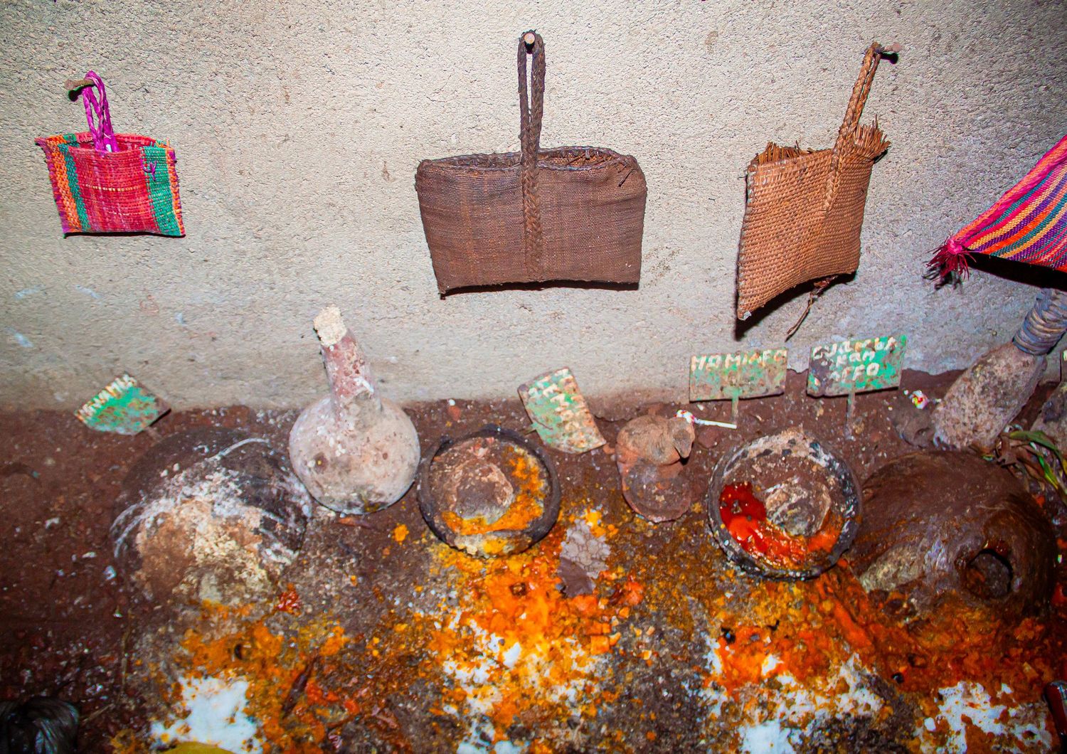 A traditional African shrine with clay pots, orange powder, red pigments, and woven baskets on a wall.