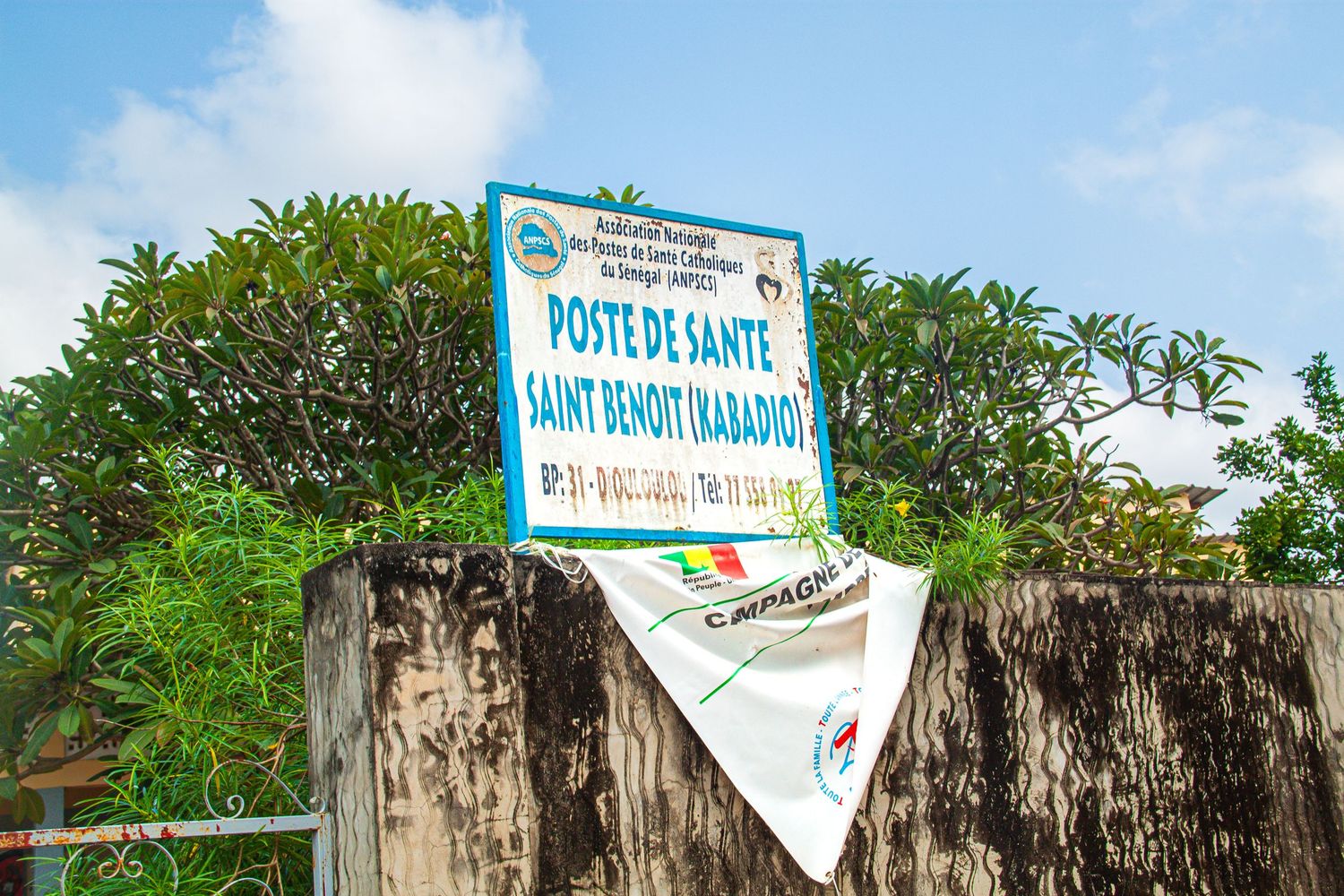 Blue health post sign reading Poste de Sante Saint Benoit Babadio mounted on weathered concrete wall.