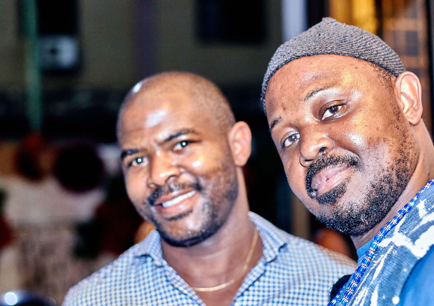 Two smiling African men pose closely together for a portrait photo at an indoor event.