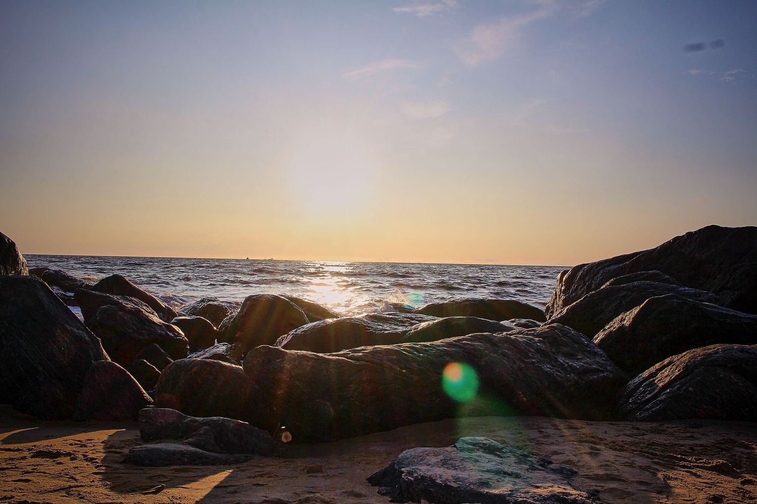 Golden sunset over rocky beach shoreline with lens flare and calm ocean waves.