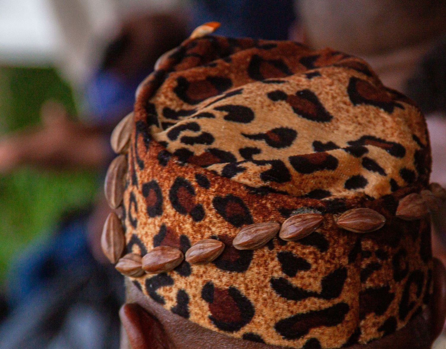 Close-up of a traditional African leopard print hat decorated with brown seeds at a cultural ceremony.