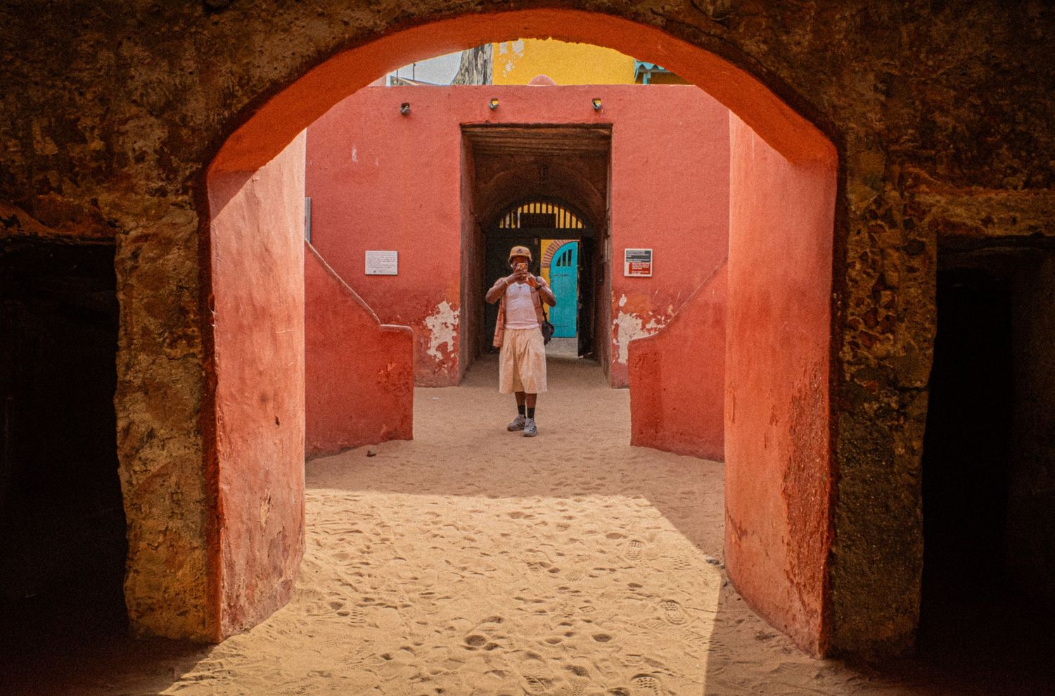 Person walking through vibrant red arched doorways of historic Goree Island slave house.