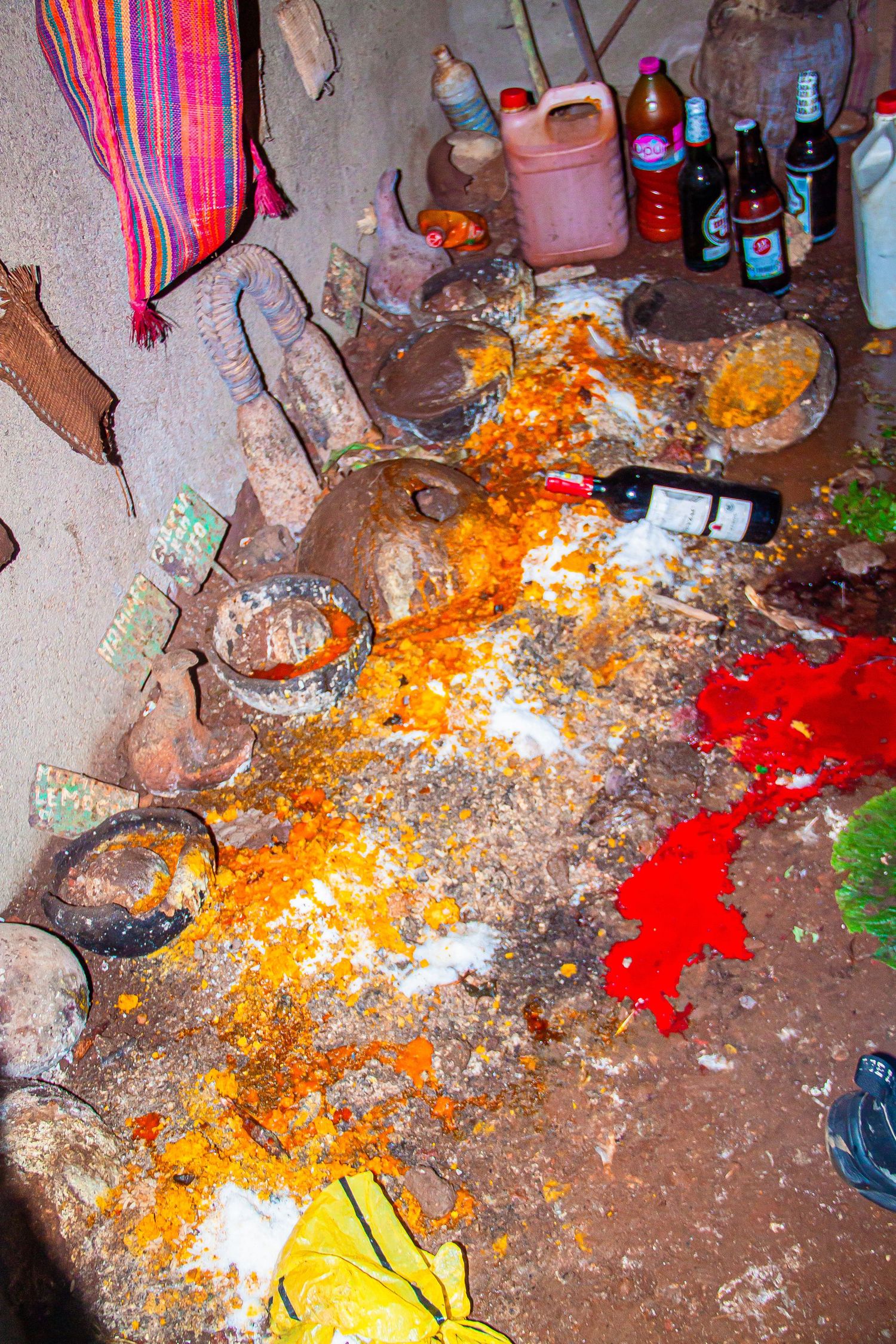 A traditional African shrine floor covered with orange powder, red pigments, bottles, and ritual offerings.